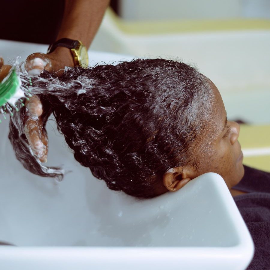 A stylist detangling a client's wet curls with a brush at the basin